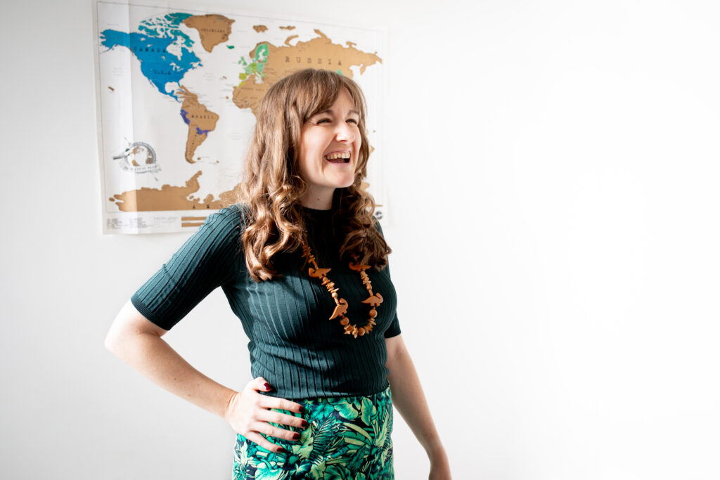 Lindsay laughing in green outfit with world map behind